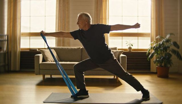 Senior man performing resistance band lunge indoors improving balance and strength at home