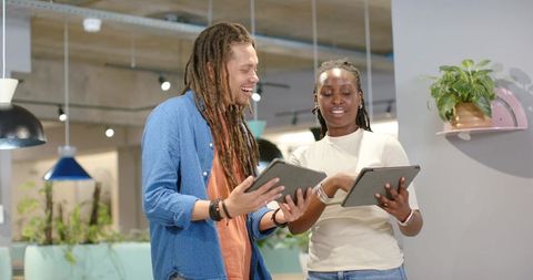 Young Professionals Collaborating on Tablets in Modern Open-Plan Office with Greenery