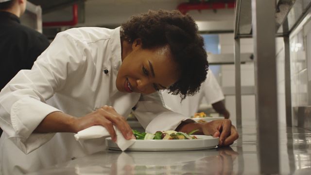 Chef is focused while adding finishing touches to a dish in lively restaurant kitchen. Perfect for editorial pieces on professional kitchens, culinary skills, or showcasing restaurant staff working environment.