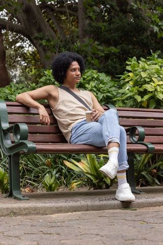 African american man relaxing on park bench holding coffee cup