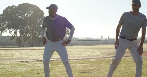 Backlit baseball teammates warming up on sunlit grass field during early morning practice