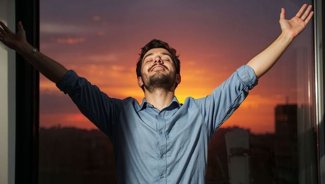 Young man stretching at sunset in highrise office embracing evening freedom