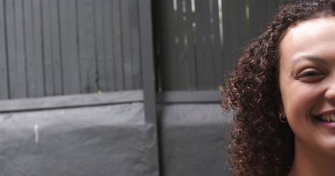 Smiling african american woman with curly hair and hoop earring against gray fence