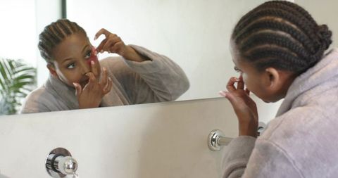 African american woman placing contact lens in mirror during morning grooming routine