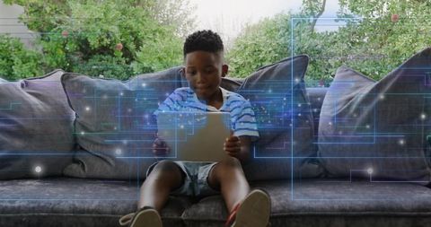 Child exploring digital learning on tablet sitting on sofa with holographic blue overlay