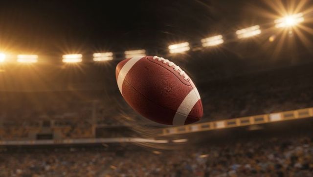 Spinning american football arcing through crowded stadium night under dramatic floodlights