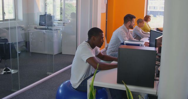 Individuals from diverse backgrounds working at desks in a modern office. This image shows teamwork, collaboration, and productivity with a mix of modern furniture and technology. Ideal for use in corporate materials, business websites, and articles on office environment and professional settings.
