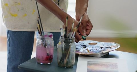 African American artist squeezing vibrant paint onto palette preparing brushes in sunlit studio