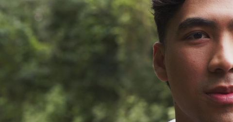 Closeup half-face portrait young asian man in park with soft green bokeh and left copy space