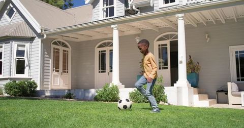 African american boy playing soccer on sunny suburban lawn by classic porch columns