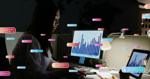 Woman reviewing financial charts late night in office cubicle with digital data overlays