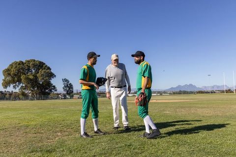 Coach Instructing Two Baseball Players During Practice on Sunny Field With Mountain View