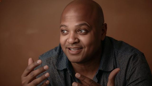 Smiling man gesturing while speaking, warm intimate portrait with soft brown background