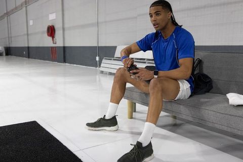 Young athlete resting on bench inside gym holding shaker bottle wearing blue shirt and white shorts