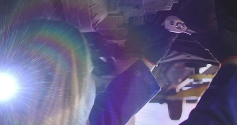 Female mechanic working under vehicle lift holding ratchet wrench backlit with lens flare