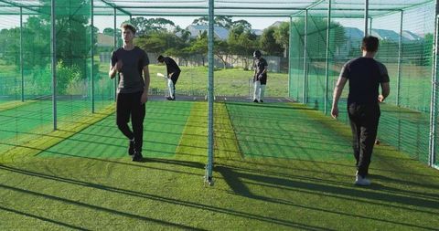 Cricket players training in outdoor nets practicing batting and fielding under sunlight