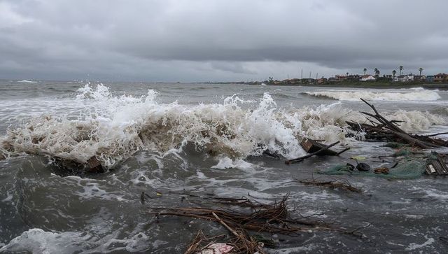 Stormy waves crashing on driftwood-strewn shoreline near coastal village