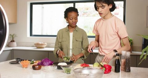 Diverse couple chopping and mixing fresh salad on bright marble kitchen island with avocado