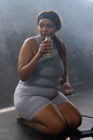 Black woman kneeling, drinking from glass bottle after workout in grey activewear