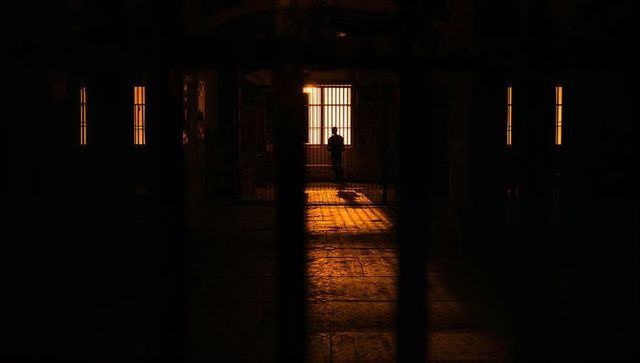 Silhouette of Man Standing at Confined Window with Barred Gate