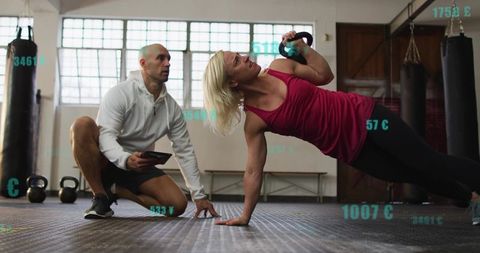 Female athlete performing kettlebell side plank while trainer tracking progress on tablet