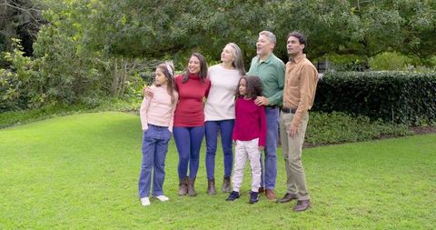 Multigenerational diverse family posing outdoors under tree in casual sweaters and jeans