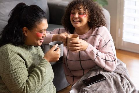 Diverse women enjoying cozy self-care moment with under-eye patches holding warm mugs