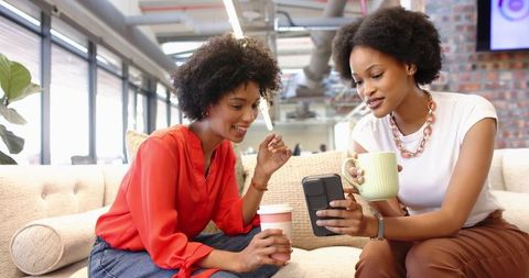 African american women in office lounge discussing on smartphone