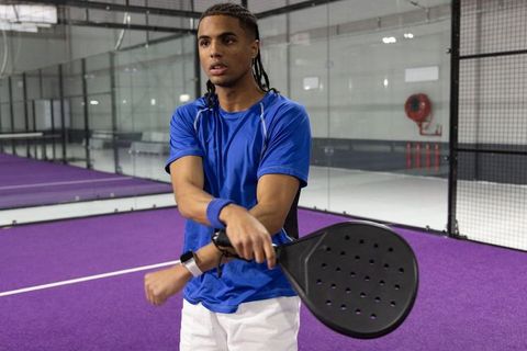 African american athlete practicing padel on purple indoor court holding black paddle