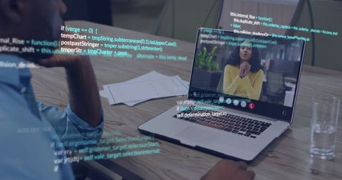 Developer joining video call while reviewing code on laptop at modern office table