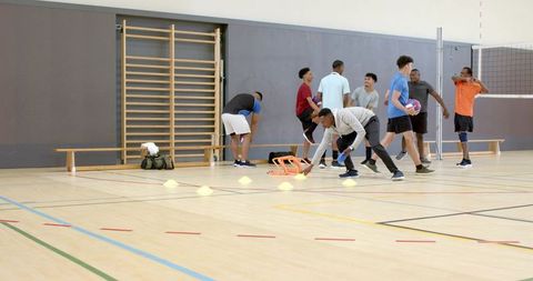 Diverse male teammates placing cones and warming up for volleyball practice in school gym