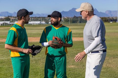 Coach gesturing and instructing two baseball players during outdoor practice