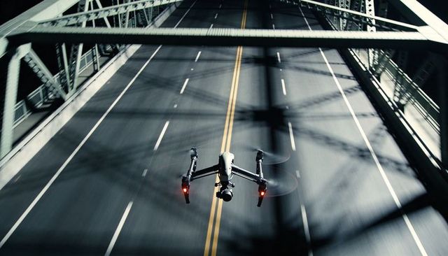 Hovering drone over truss bridge with spinning props, red navigation lights, motion blur