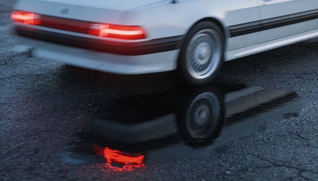White sedan sliding on wet asphalt at dusk with vivid taillight reflection in puddle