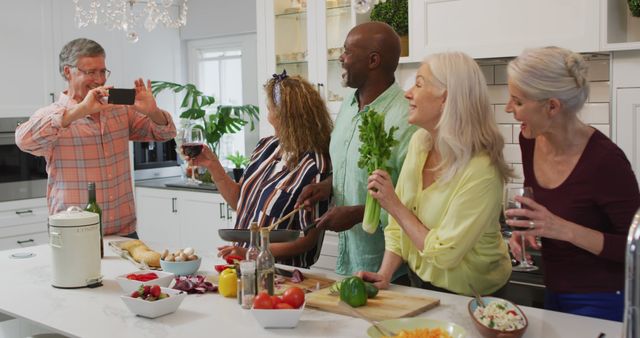 Image of happy diverse female and male senior friends preparing meal, taking photo. retirement lifestyle, spending quality time with friends and technology.