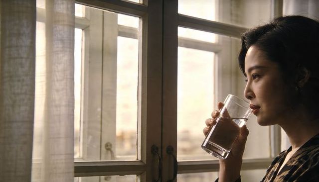 Contemplative woman sipping water by sunlit paned window, serene warm light, morning calm