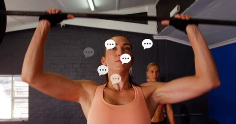 Female athlete pressing loaded barbell overhead while training in gym with speech bubbles