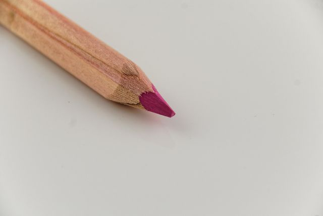 Wooden colored pencil with a pink tip on white background, ideal for educational materials, artistic projects, or design tool advertising. Perfect for illustrating creativity, school supplies, or artistic themes in various visual media.