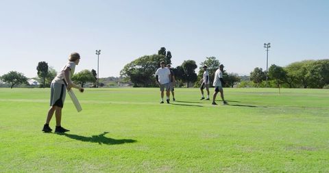 Diverse men playing cricket on sunny park field practicing teamwork and casual sport