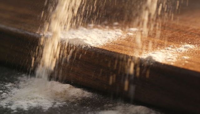Falling flour dusting wooden cutting board creating warm highlights motion closeup