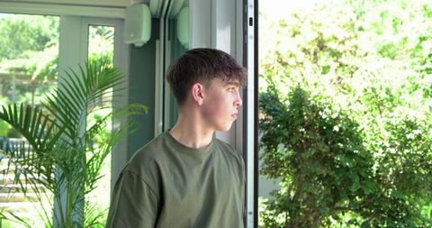 Teen standing by sliding glass door looking toward lush garden with potted palm