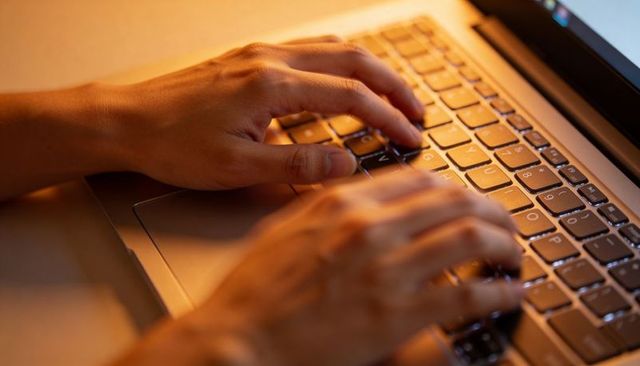 Warm orange-lit hands typing on laptop keyboard closeup remote work coding productivity