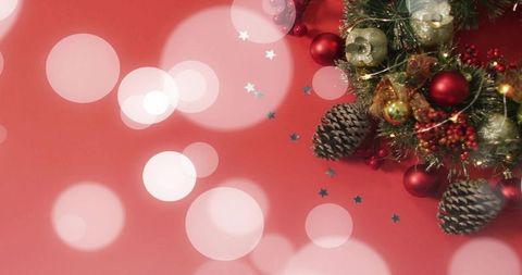 Christmas wreath with pine cones, red ornaments and glitter ribbons on bokeh red backdrop