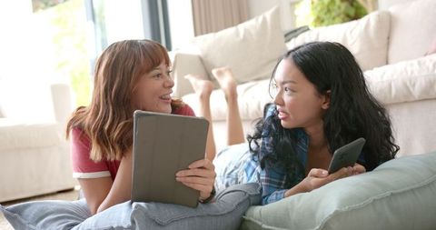 Biracial Female Friends Lounging with Tablet and Smartphone, Cozy Living Room