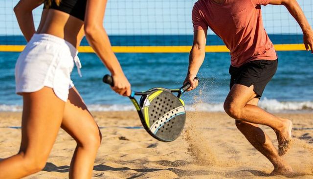 Pair playing beach paddle tennis on sunny sand court with ocean horizon