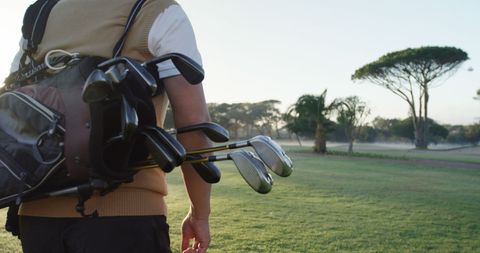 Golfer walking on course with golf bag in early morning light
