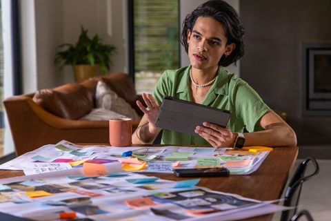 Asian man planning project at home desk using tablet surrounded by colorful sticky notes