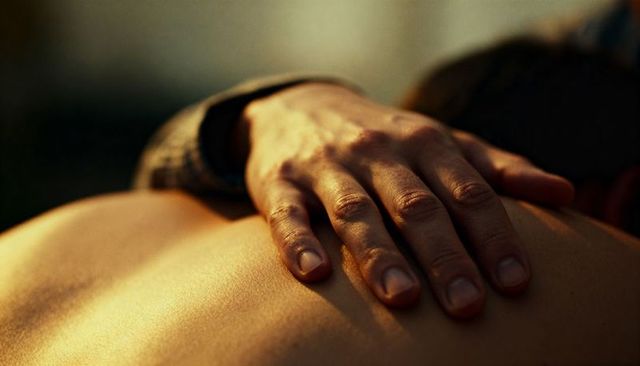 Gentle hand resting on bare shoulder, warm golden glow conveying intimate tenderness closeup