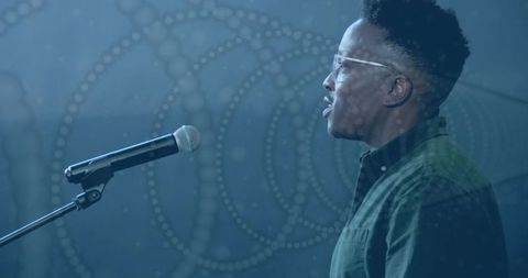 Vocalist singing into microphone under moody blue projection with circular dotted pattern