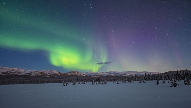 Aurora borealis dancing over snowfield and mountain range under starry arctic sky
